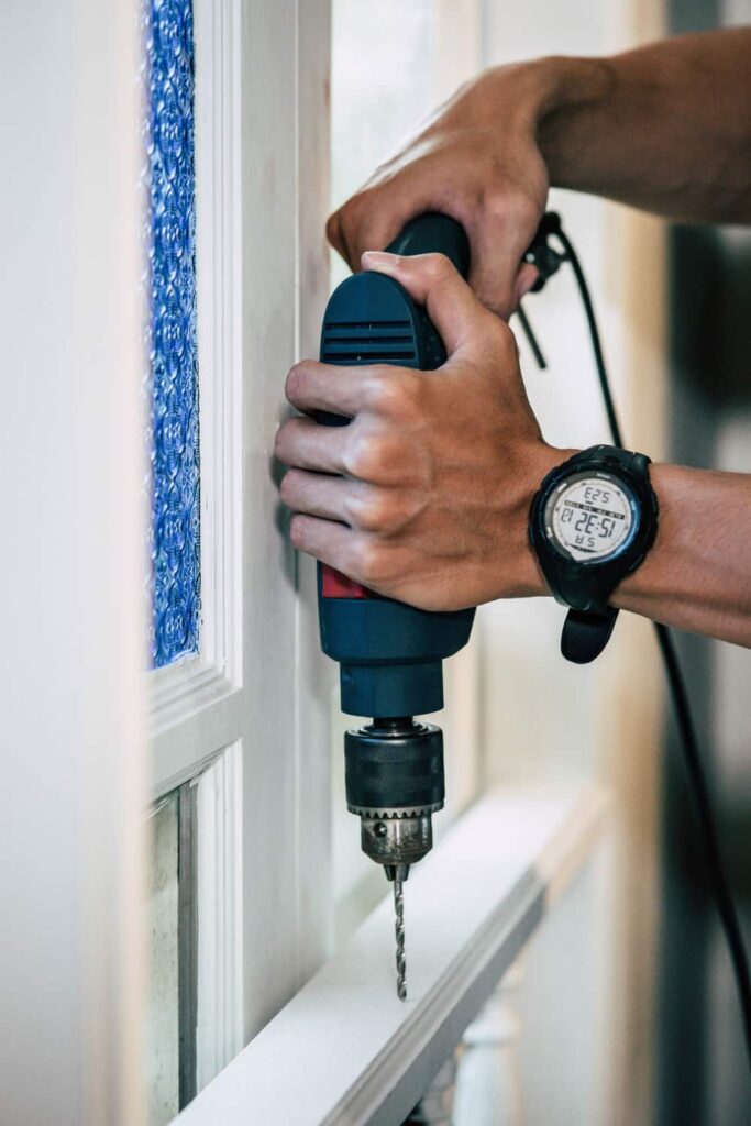 A drill drilling a screw into the window sil.